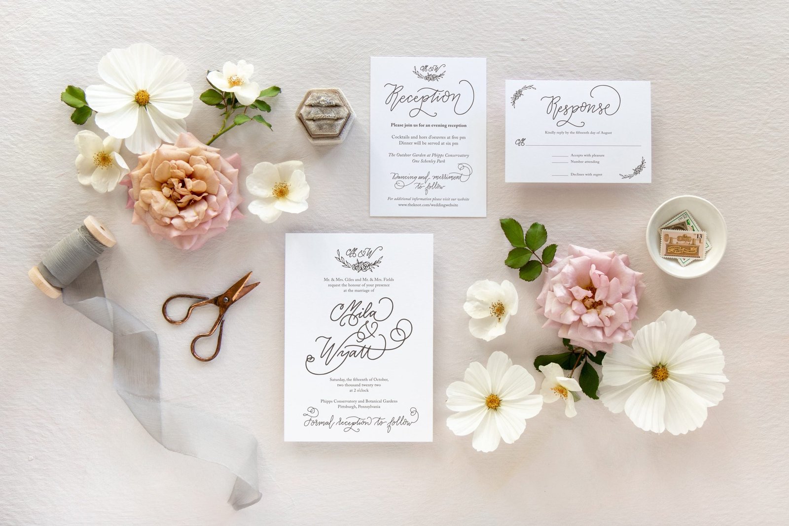 3 piece wedding invitation suite laid out flat surrounded by flowers and trinkets