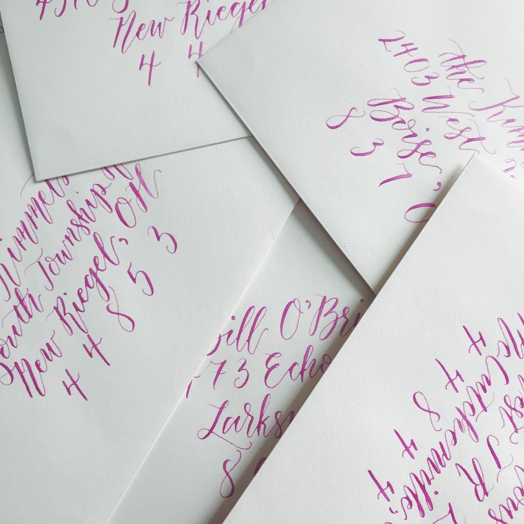 Stack of white envelopes with envelope calligrapher done with pink ink in a whimsical and flowing style